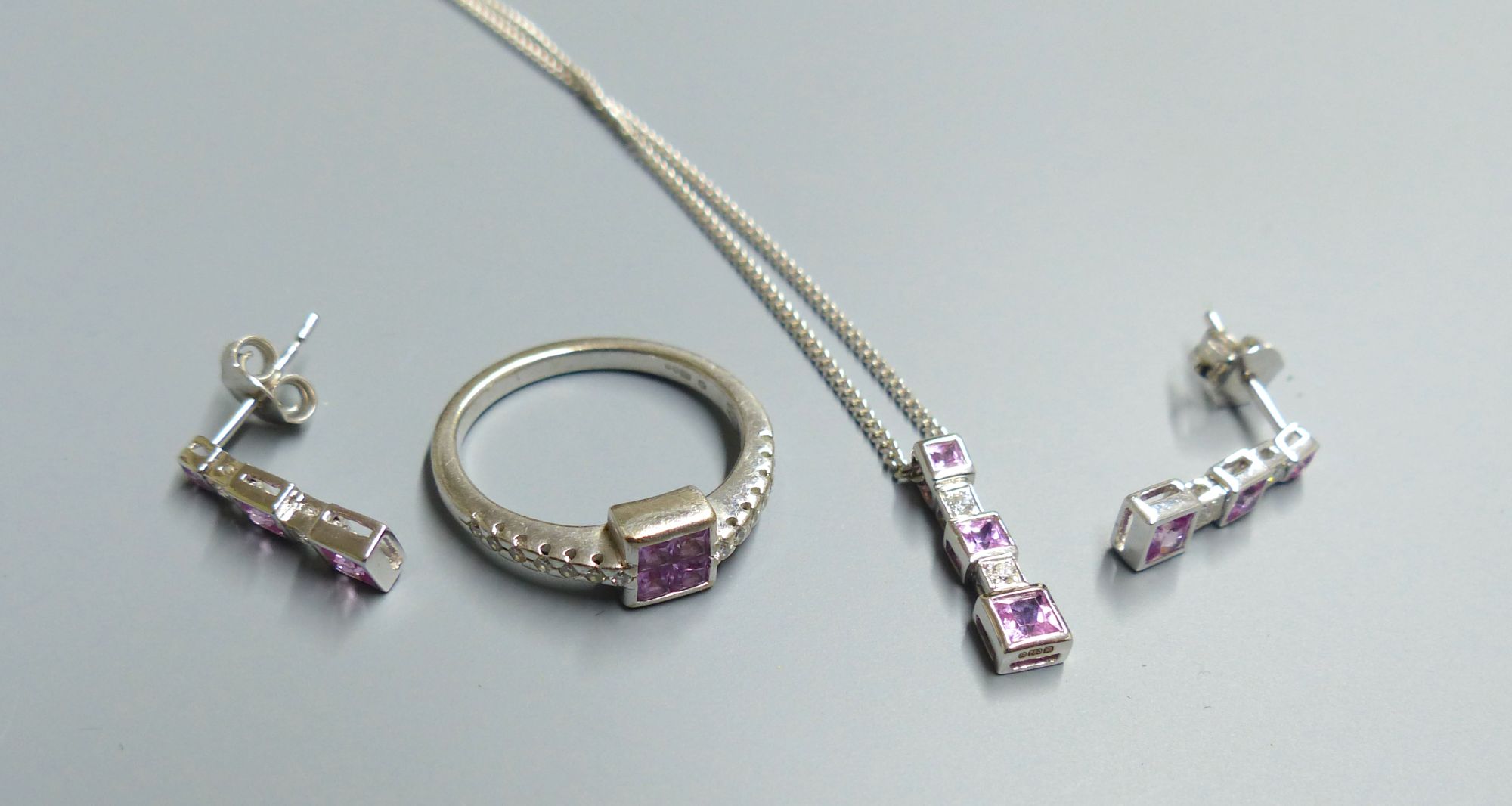 A modern 18ct white gold, pink sapphire and diamond set line pendant, on 18ct white gold chain & a pair of matching earrings